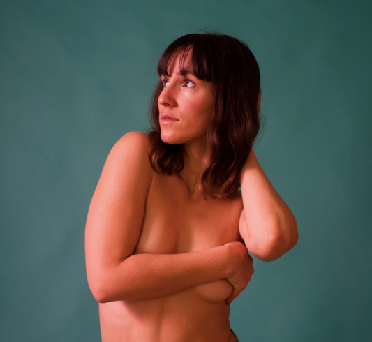 How to Give Yourself a Self Breast Exam - Nude Model Covering Breasts with Arm on Aqua Background
