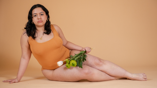 Model in orange body suite holding white flowers