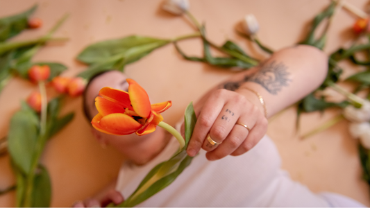 Me and My Outie Vagina Against the World - Closeup of model in white tank top holding an orange flower
