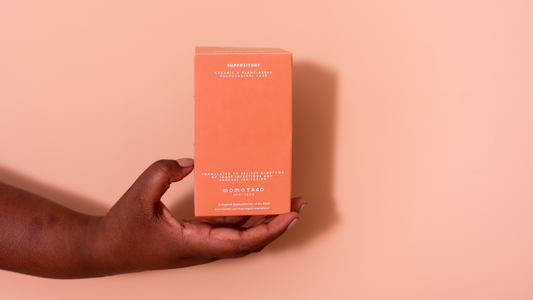 Model's hand holding  Momotaro Apotheca Organic Suppository for yeast infections and vaginal discomfort on light pink background