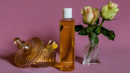 Plant based body oil sits next to beautiful roses in the Momotaro Apotheca shop for organic vulva and vaginal care. 
