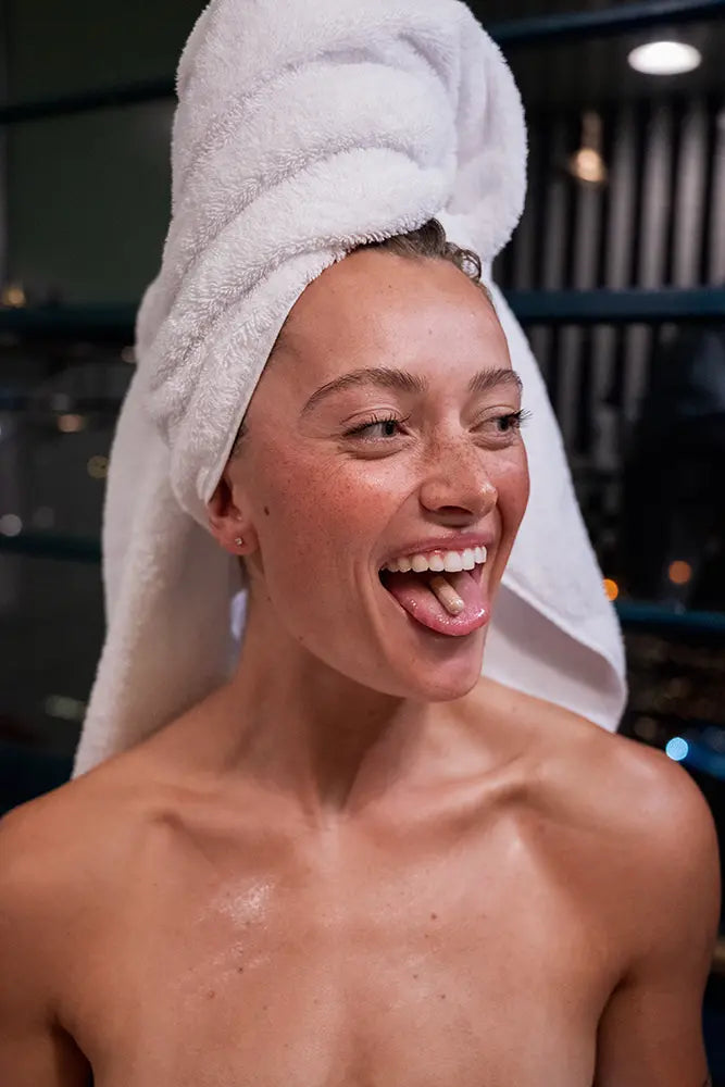 Person with a white towel on their head, sticking out their tongue with Momotaro Apotheca's UTI supplement. 