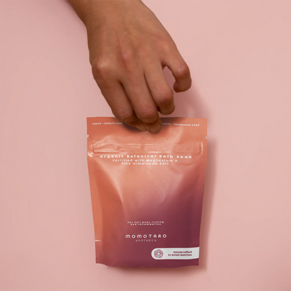 Hand reaching for Momotaro Organic Bath Soak bag on a pink background