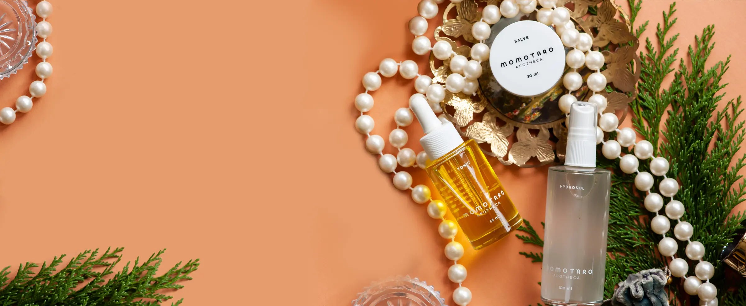 Momotaro Apotheca Products with a decorative background featuring pearls and greenery on an orange background