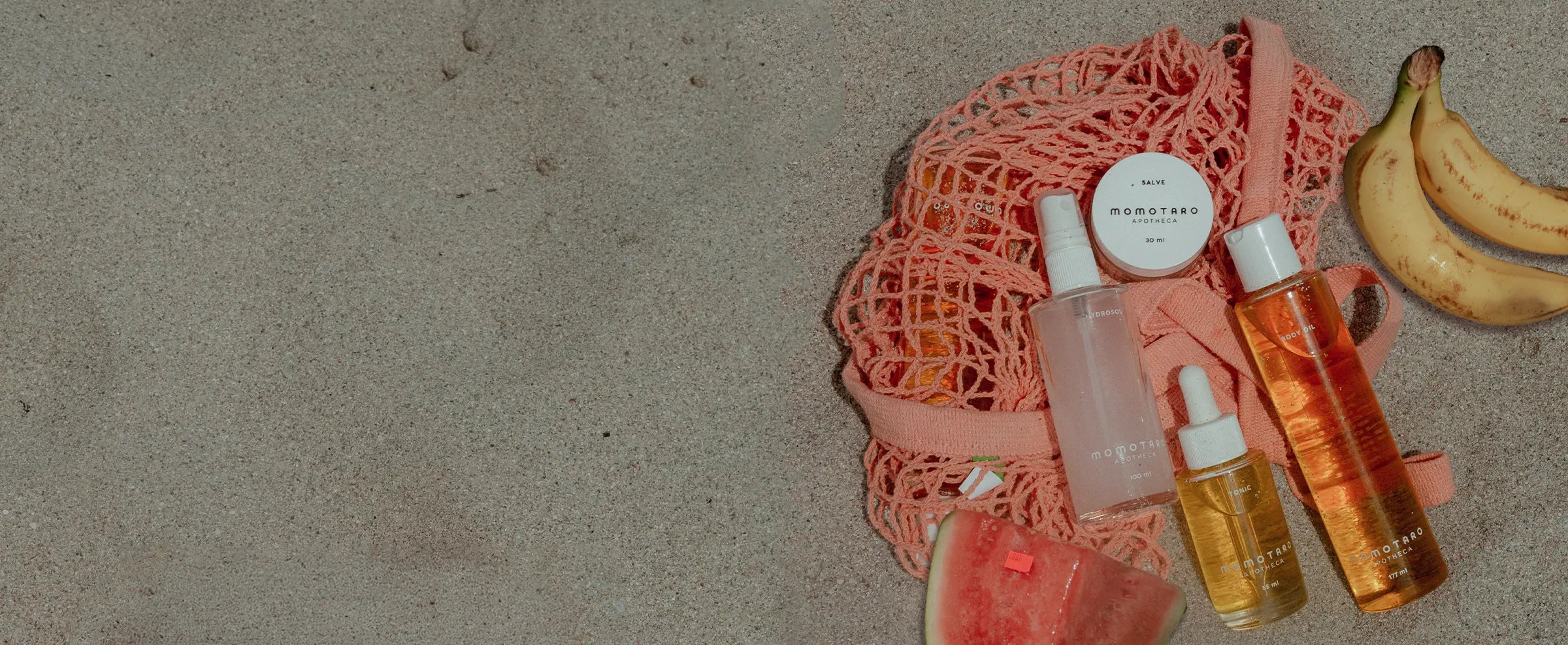 Momotaro Apotheca products and a mesh bag on the beach with bananas in the background