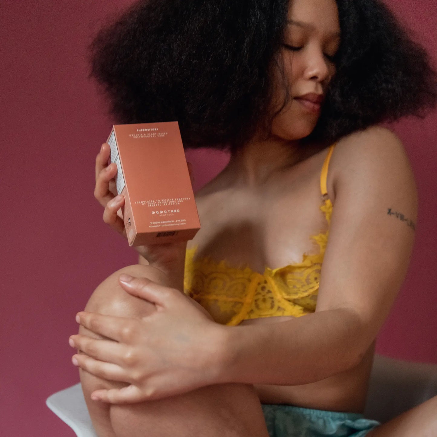 Woman holding a suppository box against a pink background.