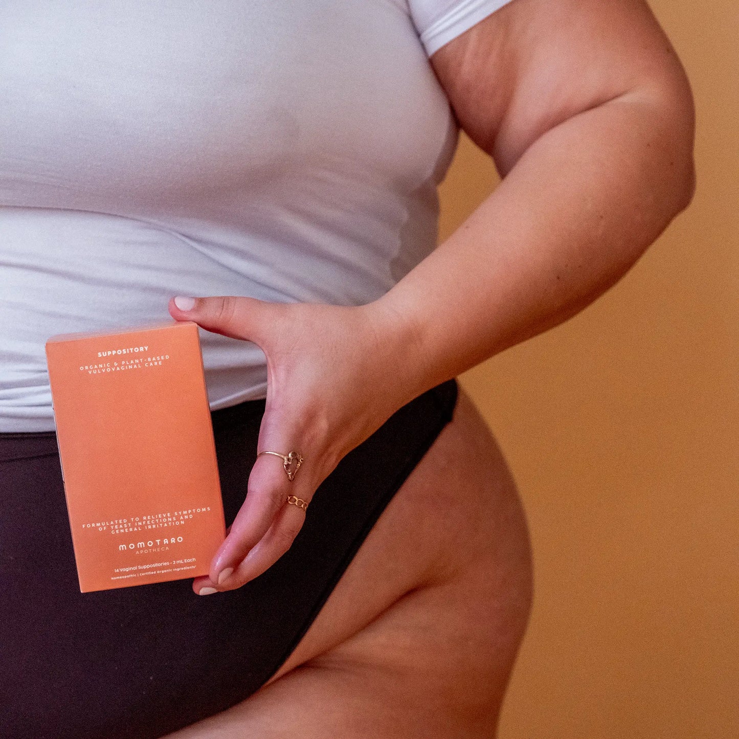 Person holding a Momotaro Apotheca Suppository box against a brown background.